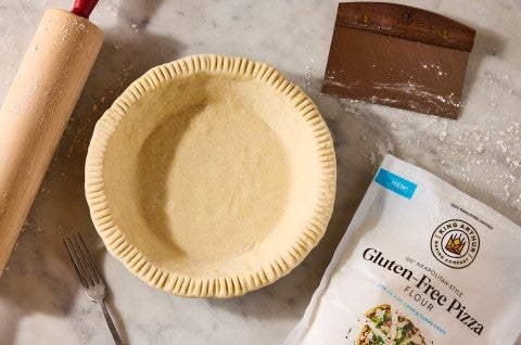 A rolling pin, pie crust, pastry knife, and bag of King Arthur Gluten-Free Pizza Flour shown on a counter and neatly arranged. - select to zoom