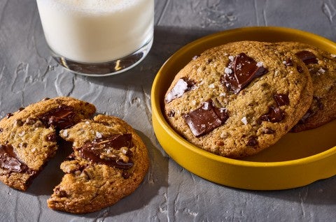 Beautifully baked High-Altitude Chocolate Chip Cookies shown on a plate and counter with a glass of milk in the background. - select to zoom