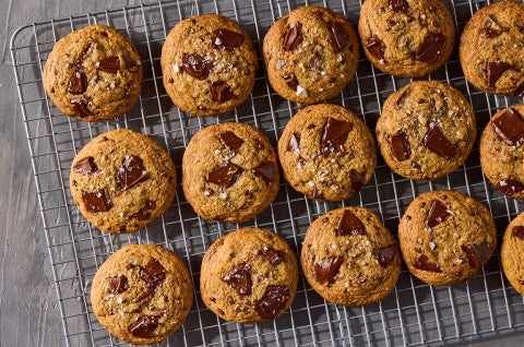 Several beautifully baked High-Altitude Chocolate Chip Cookies shown on a plate and counter with a glass of milk in the background. - select to zoom