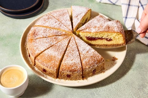 A hand removing a slice of Jelly Doughnut Cake from a plate. You can see the inside of the slice with a golden interior and lovely jelly filling. - select to zoom