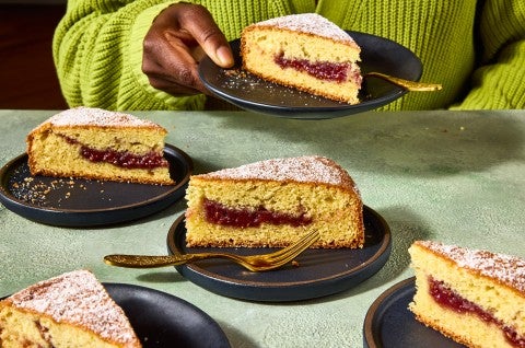 Multiple slices of Jelly Doughnut Cake arranged on a counter with a person in the background holding a plated slice. - select to zoom