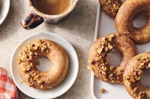 A Maple Donut on a plate with half coated in broke nut meat and the other half glazed. - select to zoom