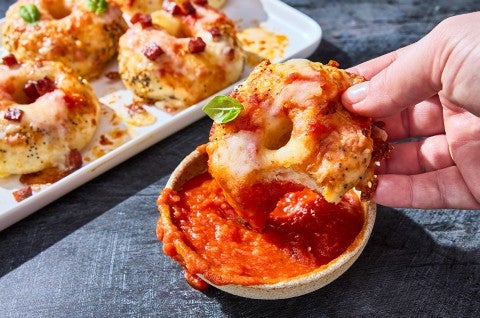 Dipping a mini pizza bagel into a small bowl of marina. - select to zoom