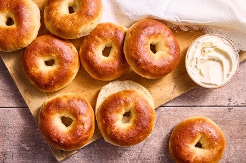 Several bagels laid out on a cutting board with a tub of cream cheese in the upper right corner of the frame. - select to zoom
