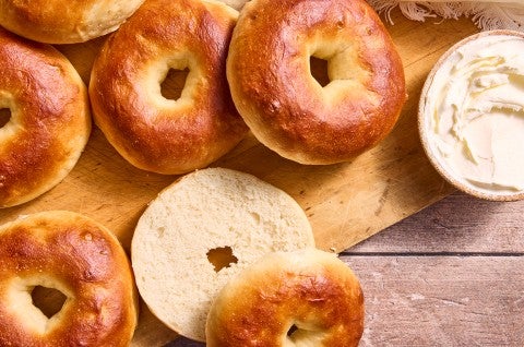 Multiple bagels on a cutting board with one sliced showing the golden interior and perfectly baked brown exterior. - select to zoom