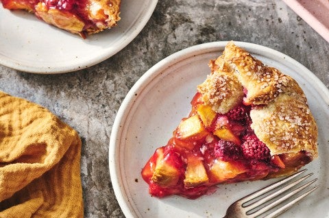 A slice of Rustic Raspberry-Peach Pie with a folded crust over the edge and vibrant fruit filling. - select to zoom