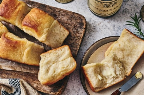 Looking down on a spread of of small-batch parker house rolls - one open on a plate with butter and others on a wooden cutting board. - select to zoom