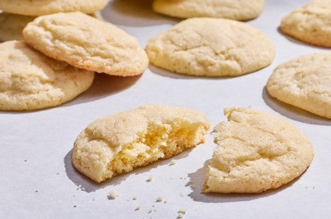 Sourdough Sugar Cookies laid out on a counter showing one of the cookies split in half with a slightly cakey interior and crumbs. - select to zoom