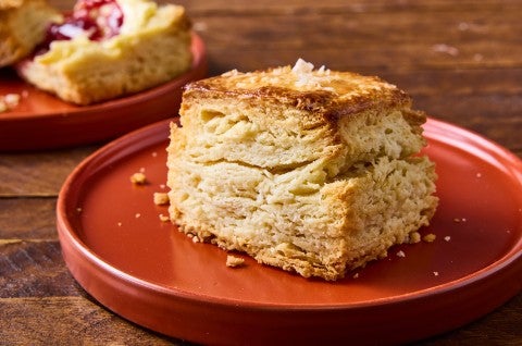 Side view of a tall ultimate flaky biscuit that clearly shows horizontal layers in the biscuit, a perfect golden baked exterior, and a bit of salt on top. - select to zoom