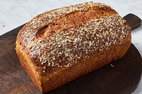 A loaf of Multigrain Protein Bread on a dark brown cutting board. - select to zoom