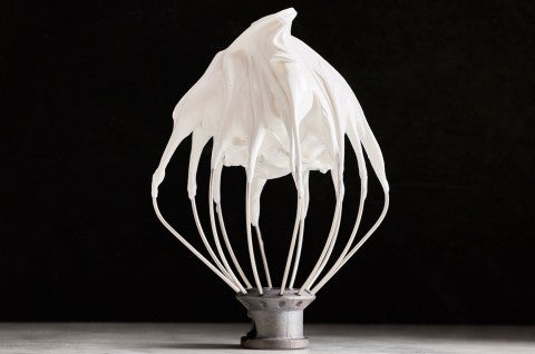 White Swiss Meringue on a mixer whisk shown upright against a black background. - select to zoom