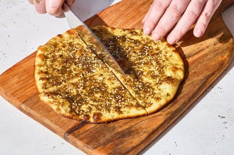 Slicing Za’atar Manakeesh ona. wooden cutting board. - select to zoom
