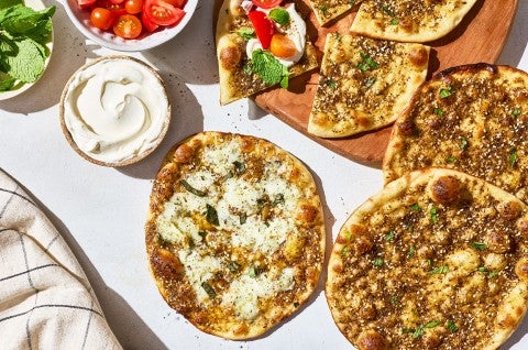 Za’atar Manakeesh spread out with toppings, dip, herbs, and veggies. - select to zoom
