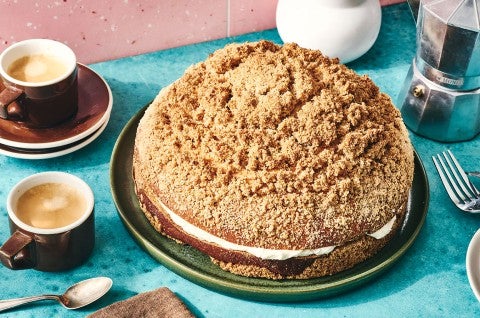 A Cream-Filled Coffee Cake on a dark plate showing a crumb top, cream edge in the middle, and coffee. - select to zoom