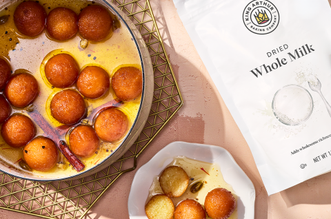 Gulab Jamun in a pot and on a plate with King Arthur Dry Whole Milk Powder in a bag next to the desert. - select to zoom