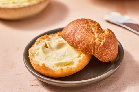 A sliced and buttered Gluten-Free roll on a small dark plate. - select to zoom