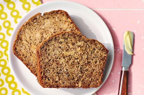 Two slices of sourdough banana bread on a plate with a buttered knife. - select to zoom