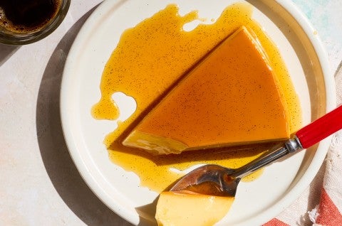 A slice of flan on a white plate with a bite on a spoon. - select to zoom