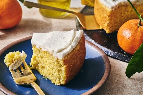 A slice of whole orange cake ona. blue plate with a bite on a fork. - select to zoom