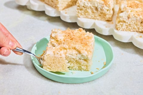 A slice of Creamy Coconut Sheet Cake on a plate with a bite on a fork - select to zoom
