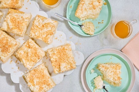 Creamy Coconut Sheet Cake arranged on a counter sliced on a platter, and additional slices on blue green plates - select to zoom