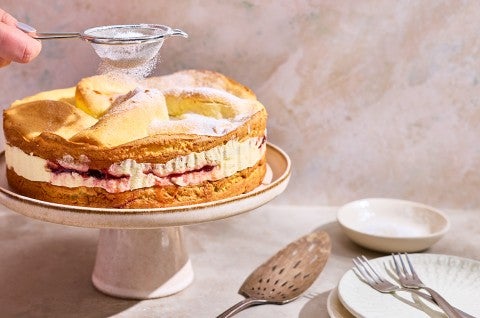 Karpatka Cake on a cake stand being dusted with powdered sugar. - select to zoom
