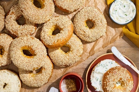 Sesame Sourdough Discard Bagels arranged on parchment with a shmear of cream cheese and a sliced bagel on a plate. - select to zoom
