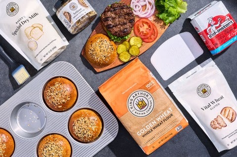 Whole Wheat Hamburger Buns in a bun pan with the ingredients to make them arranged on a counter. - select to zoom