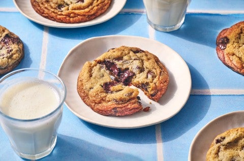 A Classic Chocolate Chip Cookie split on a plate atop a blue counter with glasses of milk in the photo. - select to zoom