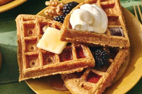 Gingerbread Waffles on a plate with whipped cream, butter, syrup, and fresh berries. - select to zoom