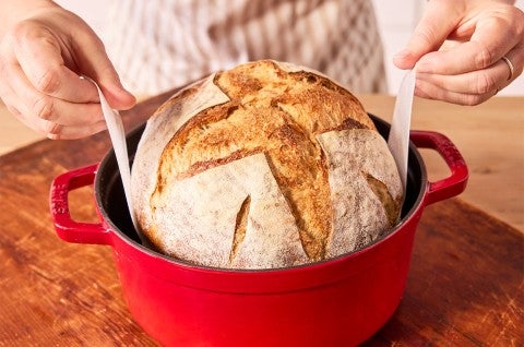 Pulling Naturally Leavened Sourdough Bread from a red cast iron crock. - select to zoom
