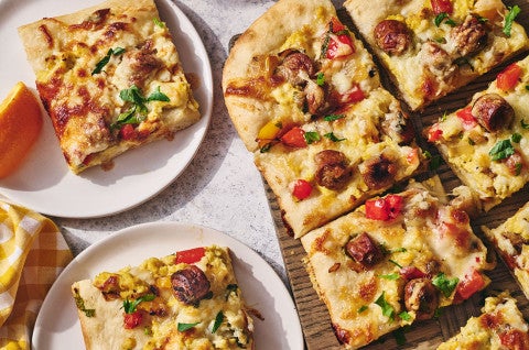 Sliced breakfast pizza on a cutting board with some slices on plates - select to zoom