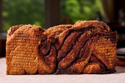 A loaf of Cinnamon Babka on a counter seen from the side with folded dough and veins of thicks cinnamon - select to zoom