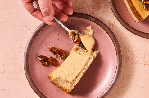 A person getting a bite of Maple Pecan Cheesecake from a slice on a pink plate - select to zoom