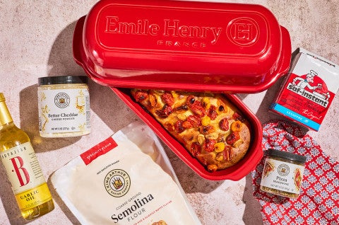 No-Knead Cheese and Tomato Garlic Bread in an Emile Henry baking pan with ingredients spread around on a counter - select to zoom