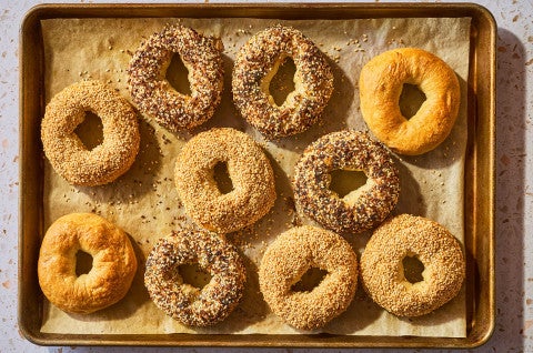 Various bagels on a sheet of parchment atop a baking pan fresh out of the oven. - select to zoom