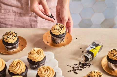 Adding sprinkles to the top of Chocolate Cupcakes with Whipped Caramel Frosting - select to zoom