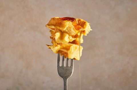 A fork with a bite of buttermilk waffles on it and syrup dripping down. - select to zoom
