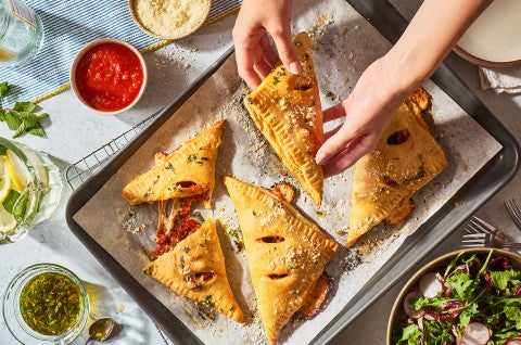 Flaky Puff Crust Pizza Turnovers on a baking sheet with someone lifting one up - select to zoom