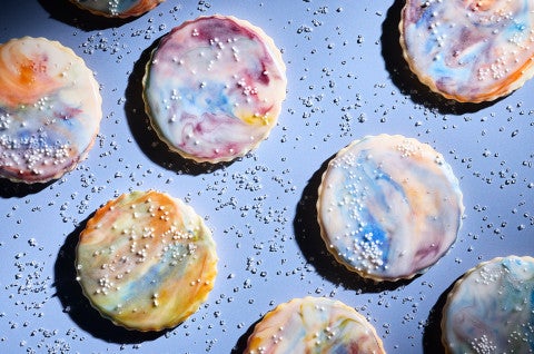 Northern Lights Iced Sugar Cookies arranged on a blue background surrounded by sprinkles of sparkling sugar - select to zoom