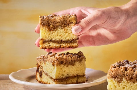 Our Favorite Sour Cream Coffee Cake stacked on a plate with a hand picking up the top slice. - select to zoom