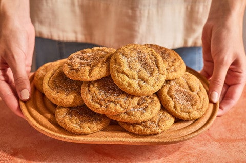 Pumpkin Snickerdoodle Cookies stacked and arranged on a plate with someone holding the plate up - select to zoom