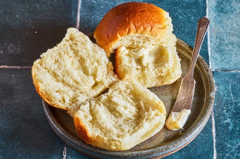 Milk bread rolls on a plate with one opened and buttered - select to zoom