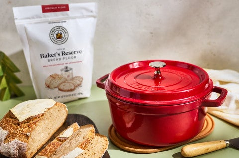 A dutch oven and a sliced loaf of crunchy sourdough with Baker's Reserve flour in the background - select to zoom