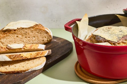Crusty Dutch Oven Sourdough Bread sliced on a cutting board and shown in a dutch oven - select to zoom