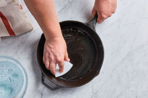 cast iron pan being cleaned with a sponge