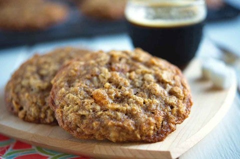 A close up side angle photo of two Oatmeal Cookies. The cookies have a crackly surface with crisp, chewy edges and soft centers. - select to zoom