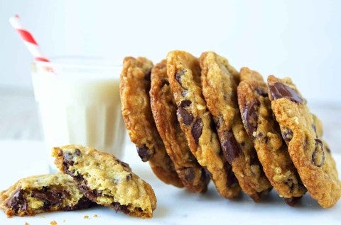 A side angle photo of oatmeal chocolate chip cookies leaning against a glass of milk. The cookies have crisp edges and chewy centers with lots of chocolate chips.  - select to zoom