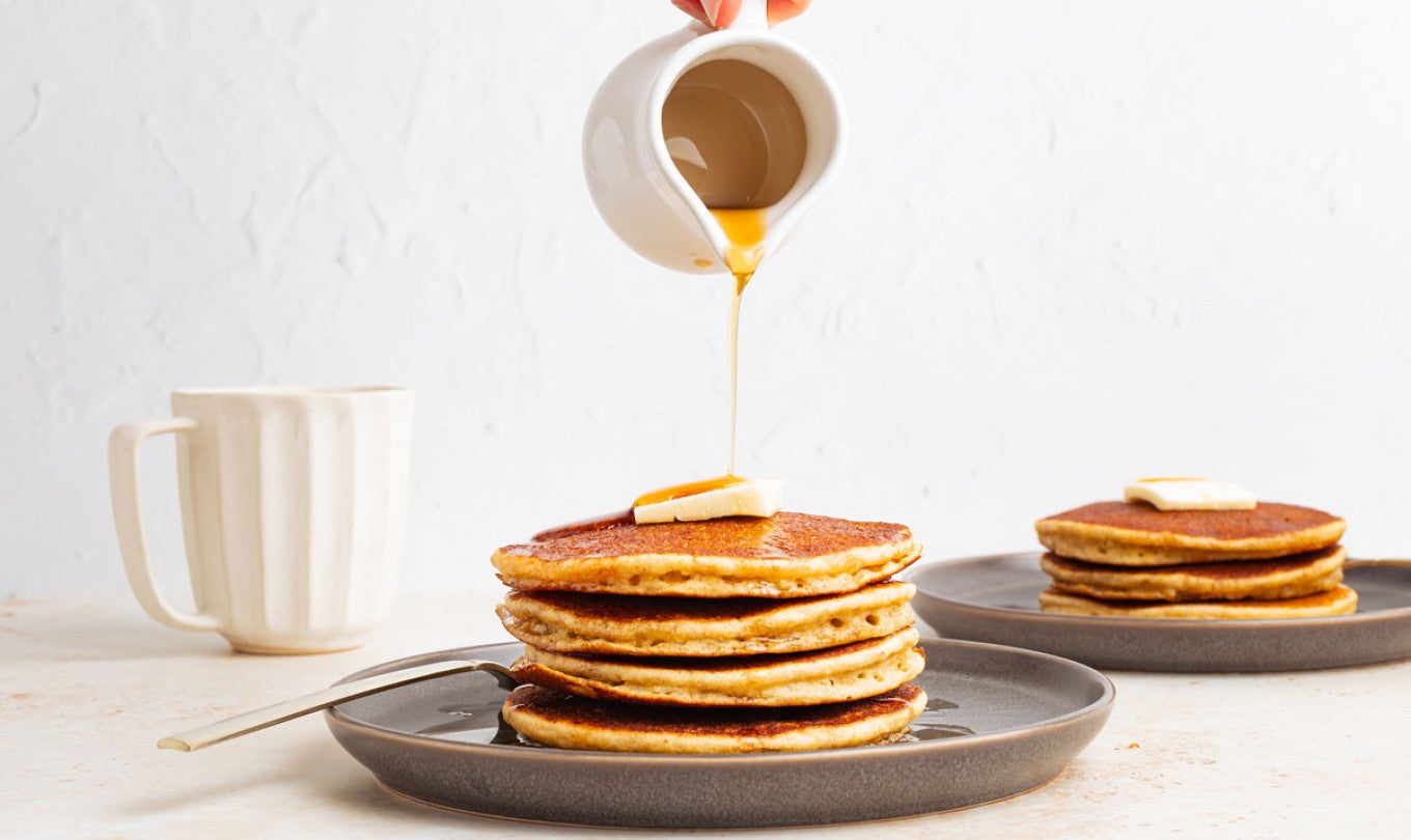 Syrup being poured onto a stack of pancakes