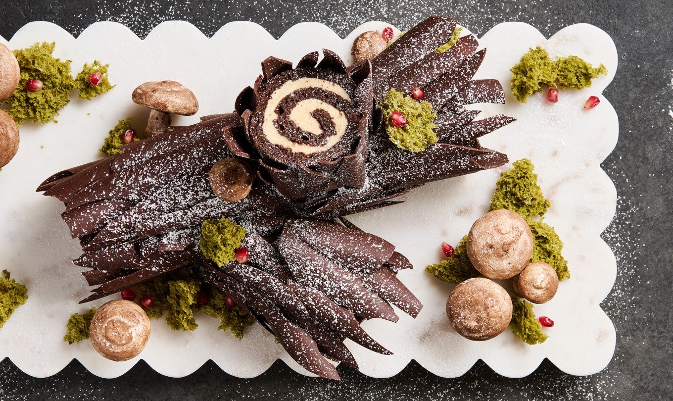 Chocolate Buche de Noel with Cookie Butter Whipped Ganache on a white cutting board sitting on a stone counter. Seen from above.